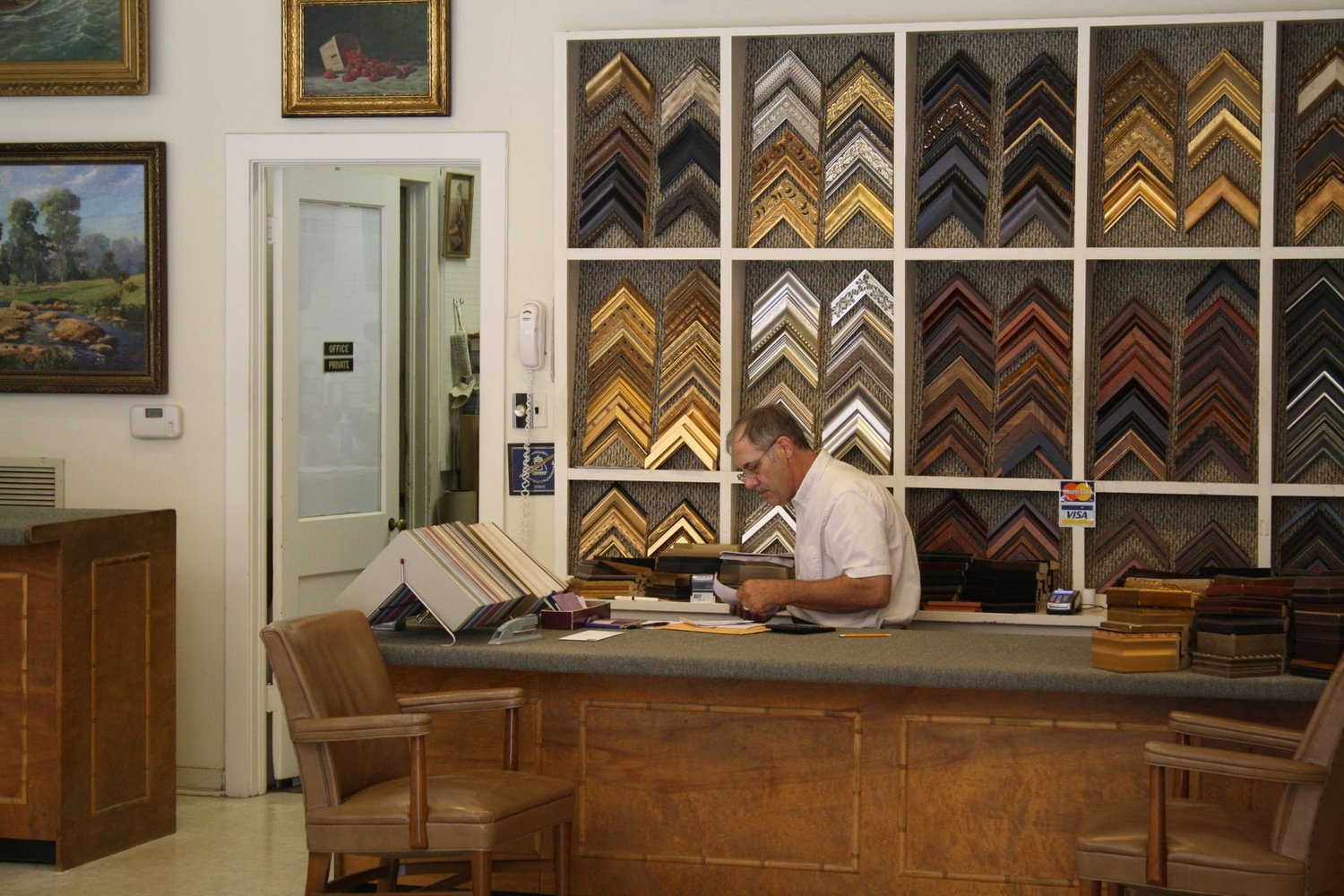 Greg Dow working at the counter in front of the wall of frame corner samples
